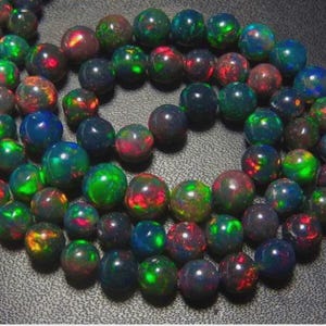 May include: A strand of round, polished opal beads. The beads display a range of colors, including green, red, blue, and black, with a shimmering, iridescent quality. The beads are approximately 0.5 inches in diameter.