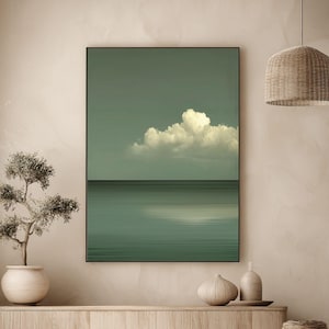 May include: A framed art print showing a tranquil seascape. The image features a muted teal sky with a fluffy white cloud above a calm, teal ocean. The print is in a black frame, creating a minimalist aesthetic.