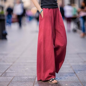 May include: Wide-leg, burgundy pants with pockets. The pants are made of a flowing fabric and are worn with a black top and sandals. The pants have a relaxed fit and a casual style.