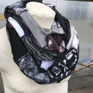 Puede incluir: Una bufanda infinita de color negro y blanco hecha de tela reutilizada. La bufanda presenta una variedad de patrones, incluyendo rayas, lunares y un diseño de calavera y huesos cruzados.