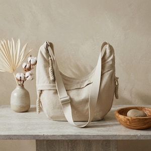 Puede incluir: Una taza de cerámica blanca con un asa negra y el texto "But First, Coffee" en un estilo manuscrito. La taza está sobre una superficie blanca. La taza mide aproximadamente 10 cm de alto.