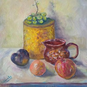 May include: Oil painting of a still life arrangement featuring a golden cylindrical container topped with green grapes, a red pitcher, and various fruits. The fruits include a plum, an orange, and a red apple. The artwork is signed in the lower left corner.