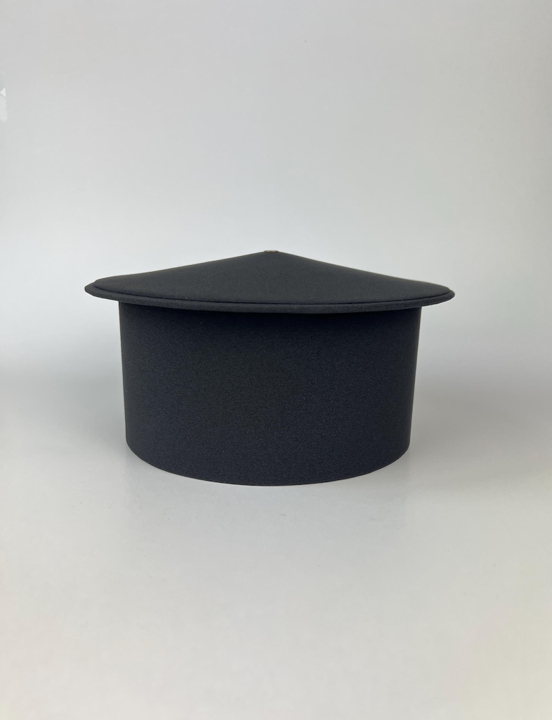 May include: A black, cylindrical hat with a triangular top. The hat has a wide brim and a textured surface. The hat is made of a soft material and is likely a costume or fashion accessory.