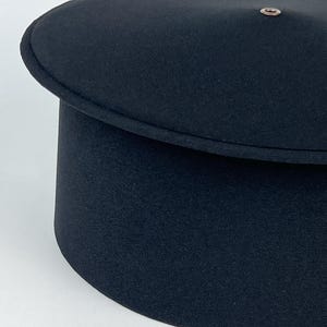 May include: A black hat with a rounded top and a cylindrical base. The hat has a small, circular metal detail on the top. The hat's design is simple and classic, suitable for various occasions.