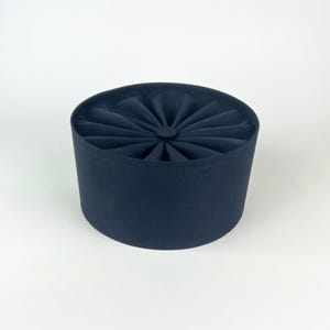 May include: A navy blue, cylindrical hat with a pleated, fan-like design on top. The hat has a rounded shape and a smooth, solid color. The hat is likely a fashion accessory.