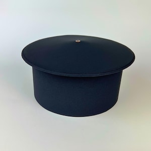 May include: A navy blue hat with a rounded top and a cylindrical base. The hat has a small, circular, gold-colored accent on the top. The hat is likely made of a soft fabric.