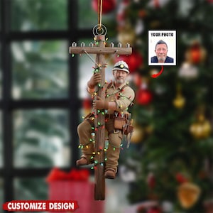 Puede incluir: Adorno navide&ntilde;o que representa a un liniero trepando a un poste de electricidad de madera adornado con luces de colores. El adorno incluye un espacio para una foto, etiquetado como "YOUR PHOTO", y el texto "CUSTOMIZE DESIGN".