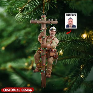Puede incluir: Adorno navide&ntilde;o que representa a un liniero subiendo a un poste de electricidad decorado con luces de colores. El liniero lleva casco, ropa de trabajo y cintur&oacute;n de herramientas. El adorno tiene una cuerda dorada para colgar y un espacio para una foto. El texto "CUSTOMIZE DESIGN" est&aacute; en la parte inferior.