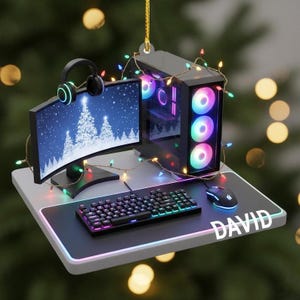 May include: A gaming PC Christmas ornament featuring a computer monitor displaying a snowy Christmas tree scene, a keyboard, mouse, and headphones. The ornament is decorated with colorful lights and the name "DAVID" is displayed on the mousepad.