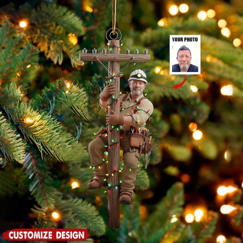 Puede incluir: Adorno navide&ntilde;o que representa a un liniero subiendo a un poste de electricidad decorado con luces de colores. El adorno incluye un espacio para una foto y el texto "CUSTOMIZE DESIGN". El liniero lleva ropa de trabajo.