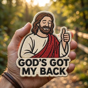 May include: Embroidered patch featuring a smiling Jesus with a thumbs-up gesture. He is depicted with brown hair and a beard, wearing a white robe and a red sash. The patch has the text "GOD'S GOT MY BACK" in black letters.
