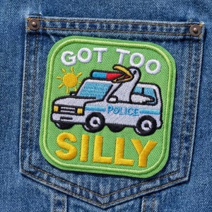 May include: A green patch with the words "GOT TOO SILLY" and a cartoon police car with a bird on top. The patch is sewn onto a blue denim pocket.