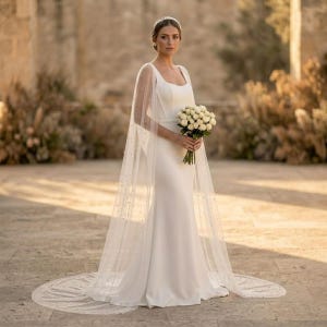 Peut inclure: Une robe de mari&eacute;e blanche avec une longue tra&icirc;ne et une cape transparente orn&eacute;e de petites perles. La robe a un design simple et &eacute;l&eacute;gant avec un corsage ajust&eacute; et une jupe fluide. Un bouquet de fleurs blanches est tenu.