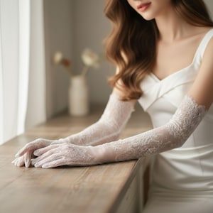 May include: Elegant, white lace gloves with intricate floral patterns. The gloves extend to the upper arm, adding a touch of sophistication. The delicate design is perfect for weddings or formal events.