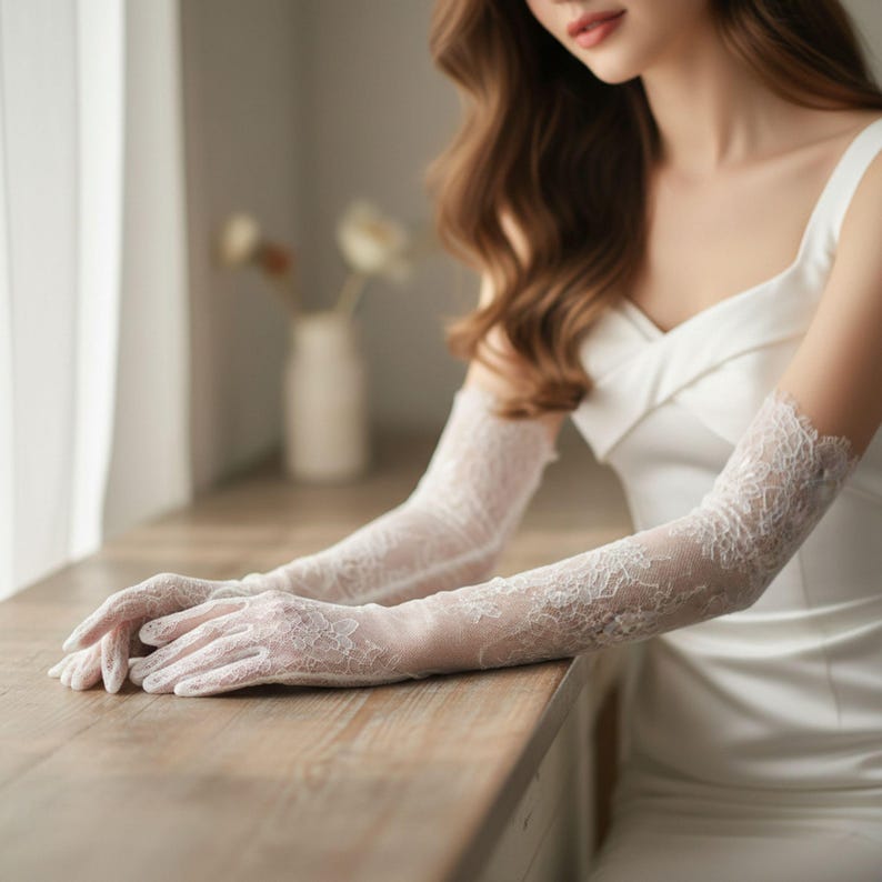 May include: Elegant, white lace gloves with intricate floral patterns. The gloves extend to the upper arm, adding a touch of sophistication. The delicate design is perfect for weddings or formal events.