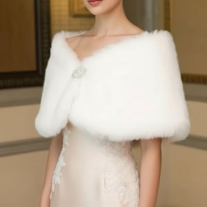 May include: A white faux fur shawl with a decorative clasp. The shawl is draped over the shoulders, creating a soft, elegant look. The clasp is a sparkling, silver-toned embellishment. This accessory is suitable for special occasions.