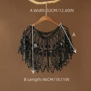 May include: Black sequined shawl with a delicate, lacy design. The shawl is 12.60 inches wide and 18.11 inches long. It is displayed on a wooden hanger against a neutral background, showcasing its intricate details and elegant style.
