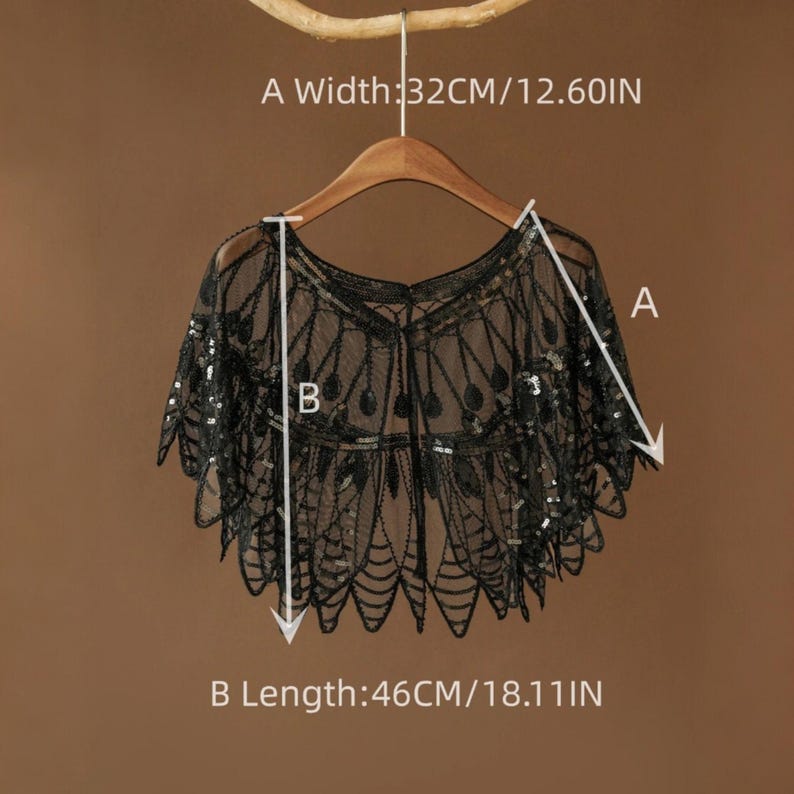 May include: Black sequined shawl with a delicate, lacy design. The shawl is 12.60 inches wide and 18.11 inches long. It is displayed on a wooden hanger against a neutral background, showcasing its intricate details and elegant style.
