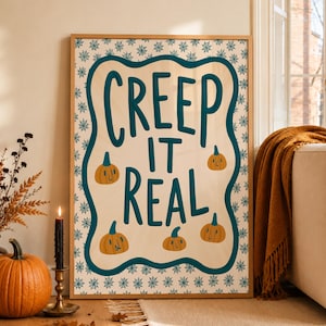 May include: A rectangular framed wall art piece featuring a cream-colored background with a dark teal wavy border and a repeating spiderweb pattern. The text "CREEP IT REAL" is printed in dark teal, accompanied by four small orange pumpkin illustrations.
