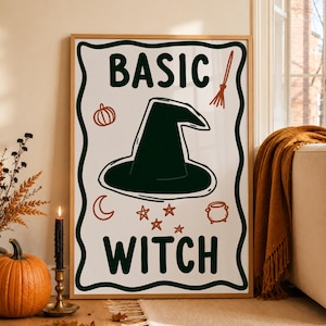 Può includere: Una stampa artistica da parete rettangolare in una cornice di legno chiaro con il testo BASIC WITCH in verde scuro. Il design include un cappello da strega verde scuro al centro, una piccola zucca arancione, una scopa, una luna crescente, stelle e un calderone.