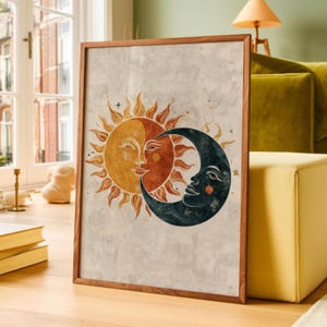 May include: A framed wall art print featuring a stylised sun and moon illustration. The sun is depicted in warm yellow and orange tones with a human face, while the crescent moon is dark blue with a face, set against a textured off-white background.