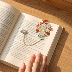 Peut inclure: Un marque-page en métal doré représentant un renard à plusieurs queues avec des détails en émail rouge, blanc, bleu et vert. L'objet se compose de deux parties reliées par une fine chaîne dorée, avec le motif du renard et une forme de nuage.