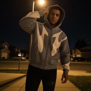 Peut inclure: Un sweat à capuche bleu clair avec une fermeture éclair et un motif de flamme blanc sur le devant et les manches. Le sweat à capuche est porté avec un pantalon noir. L'image est prise de nuit.