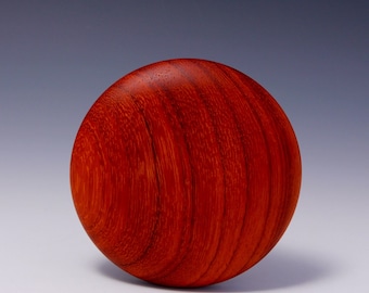 May include: A spherical object crafted from reddish-brown wood. The wood grain is clearly visible, giving a textured surface. The sphere has a smooth, polished appearance. It is likely a decorative item or a component of a larger piece. The object is evenly lit.