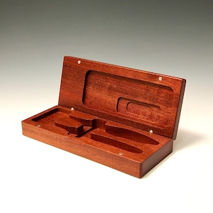 May include: A wooden box with a hinged lid, open to reveal two compartments. The box is made of a rich reddish-brown wood and has a smooth, polished finish.
