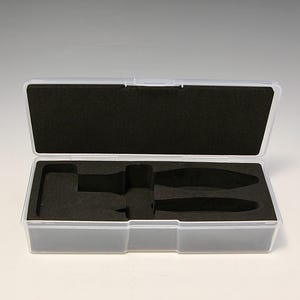 May include: A clear plastic storage case with a black foam interior. The case is open and has two empty slots for holding small items.