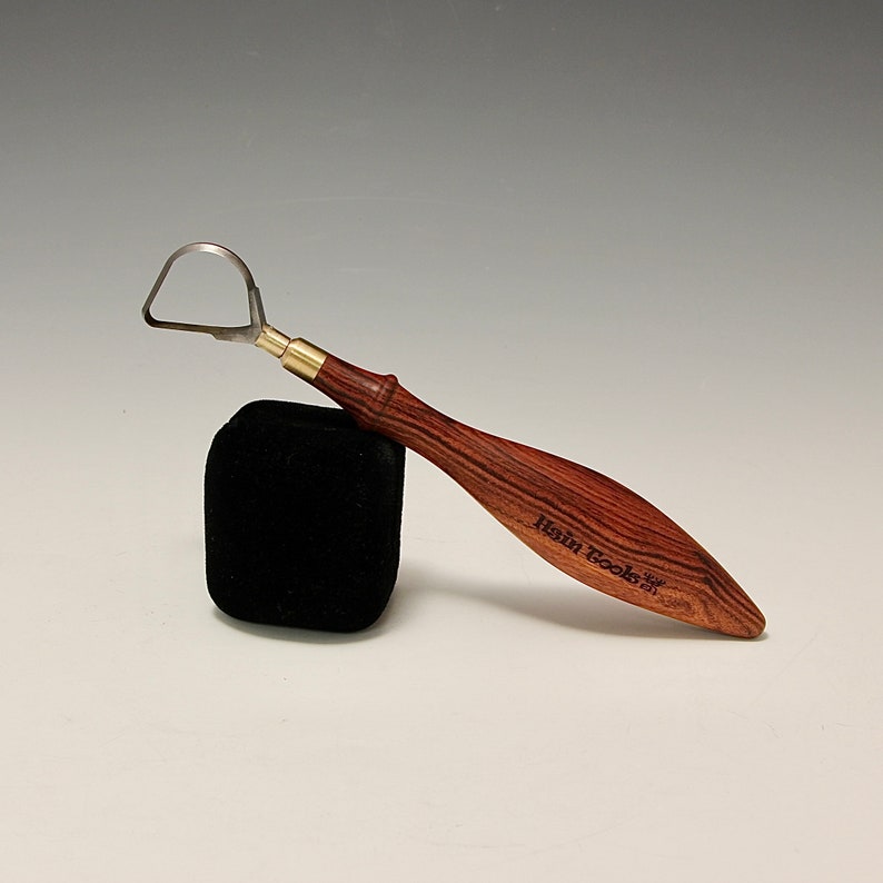 May include: A sculpting tool with a wooden handle and a metal loop at the end. The handle is dark brown with a reddish hue and has the text "Rain Tools" engraved on it.