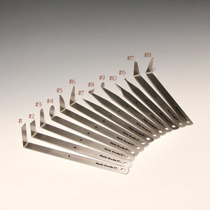 Può includere: Un set di 18 strumenti in acciaio inossidabile con punte di diverse dimensioni e forme. Gli strumenti sono contrassegnati con i numeri da 1 a 18. Gli strumenti sono disposti a ventaglio, con lo strumento più grande in alto e quello più piccolo in basso.