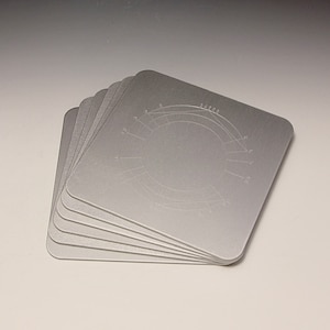 Puede incluir: Un conjunto de seis posavasos de metal plateado con un diseño circular grabado en la parte superior. El diseño incluye un círculo con líneas que irradian hacia afuera.