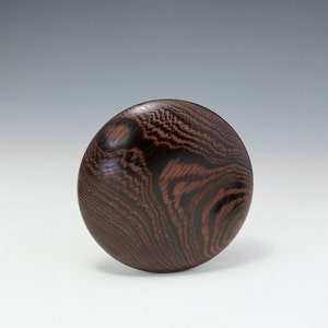 May include: A dark brown wooden bowl with a unique grain pattern. The bowl is round and has a smooth, polished finish.
