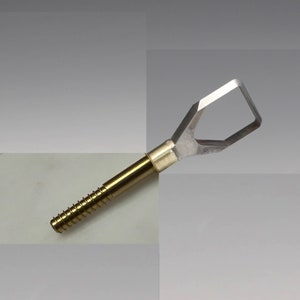 Peut inclure: Un outil de couleur dorée avec une poignée filetée et une lame en argent de forme losange. La lame a une petite ouverture au centre.