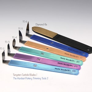 Può includere: Set di sei strumenti per la rifinitura della ceramica in carburo di tungsteno con diverse forme di lame, etichettati da TC-2 a TC-6. Gli strumenti hanno manici in plastica colorati e sono disposti in ordine di dimensione. È inclusa anche una lima diamantata.