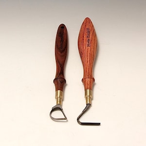 May include: Two wood-handled carving tools. One has a curved blade, the other a right-angled blade. The handles are a dark reddish-brown with brass ferrules. The tool on the right has the text "Henry Taylor" on the handle.