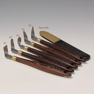 May include: Set of six palette knives with wooden handles and a diamond file. The knives are numbered 2 through 6. The file is black with a gold-colored surface.
