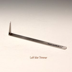 Può includere: Uno strumento di taglio a umido in metallo argentato con un'estremità appuntita e un foro all'estremità. Lo strumento è etichettato "Hair Tools ST 18". Tagliacapelli a umido sinistro.