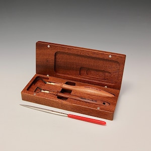 May include: A set of three wood carving tools in a wooden box. The tools have brass tips and wooden handles with the text "Hahn Tools" engraved on them. The box is made of reddish-brown wood and has a hinged lid.