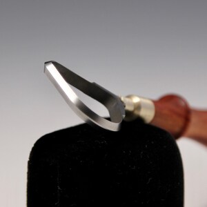 May include: Close-up of a wood carving tool with a curved blade and a wooden handle.
