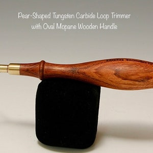 May include: A pear-shaped tungsten carbide loop trimmer with an oval Mopane wooden handle. The tool is made of metal and wood and has a brass accent.