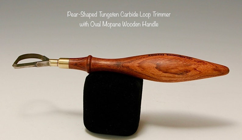 May include: A pear-shaped tungsten carbide loop trimmer with an oval Mopane wooden handle. The tool is made of metal and wood and has a brass accent.