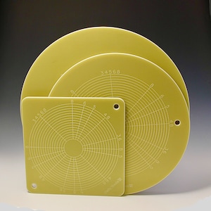 May include: Three circular, yellow-beige, ceramic protractors with white markings. The smallest protractor has a diameter of approximately 6 inches. The largest protractor has a diameter of approximately 10 inches. The protractors are marked with numbers from 3 to 8.