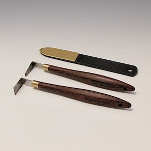 May include: Two small, angled, metal scraping tools with wooden handles. The handles are dark brown and have the text "Hein Tools" engraved on them. A black and gold metal file is also included.