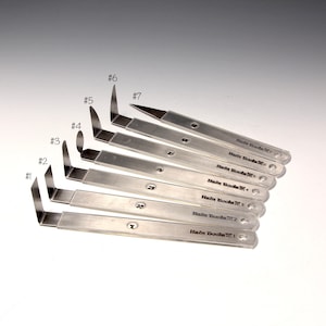 May include: A set of seven metal tools, each with a different angled blade. The tools are numbered from 1 to 7 and have the text "Hain Tools" printed on them. The tools are arranged in a fan shape.