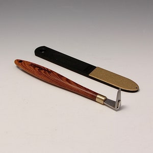 May include: A wooden handled nail cleaning tool with a metal blade and a black and gold nail file.