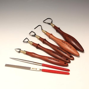 Puede incluir: Un conjunto de herramientas de cerámica con mangos de madera y cuchillas de metal. Las herramientas incluyen varias herramientas de bucle, una aguja y una lima con mango rojo. El texto "Hahn Tools" es visible en algunos mangos.