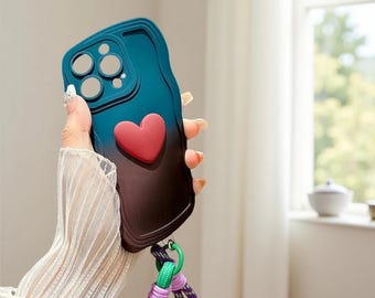 Op de afbeelding: Een teal en bruine telefoonhoes met een rood hartontwerp. De hoes heeft een gradiënteffect en een bandje met groene, paarse en witte accenten. De hoes is ontworpen om de telefoon te beschermen en een decoratieve touch toe te voegen.
