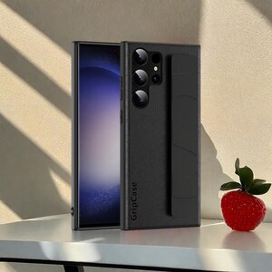 May include: Black phone case with a textured finish and a built-in grip. The case is next to a smartphone with a screen display. The case has the text "GripCase" printed on it. A red strawberry with green leaves is on the right.